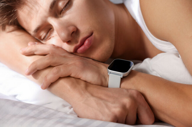 young-man-with-sleep-tracker-sleeping-on-bed-at-home-closeup