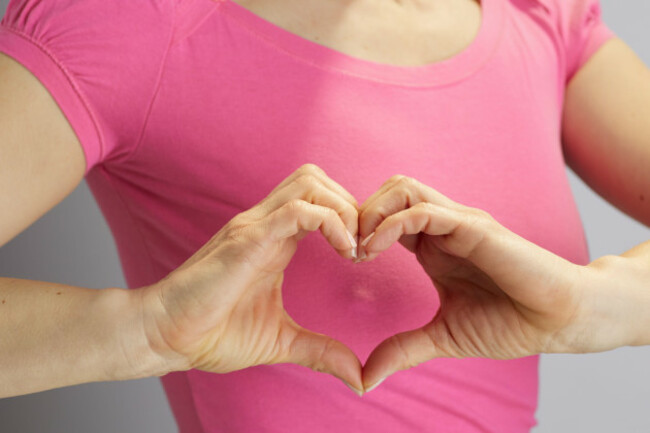 medium-close-up-of-a-woman-in-a-pink-puffed-sleeve-shirt-creating-a-heart-shape-with-her-hands-representing-compassion-support-and-womens-health-aw
