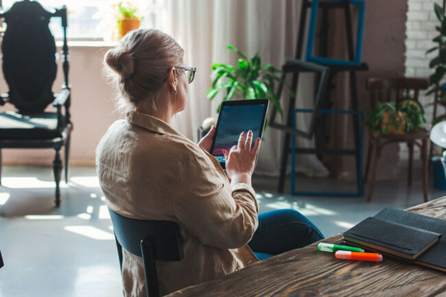 back-view-of-a-middle-aged-woman-sitting-on-chair-reading-something-from-tablet-moder-lifestyle