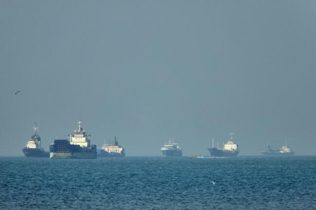 cargo-ships-including-bulk-carriers-and-general-cargo-vessels-sit-at-anchor-offshore-as-a-small-motorboat-passes-in-the-foreground-in-the-strait-of-hormuz-off-bandar-abbas-iran-monday-may-4-20