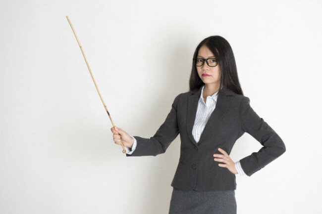 asian-female-teacher-angry-and-holding-a-stick-standing-on-plain-background
