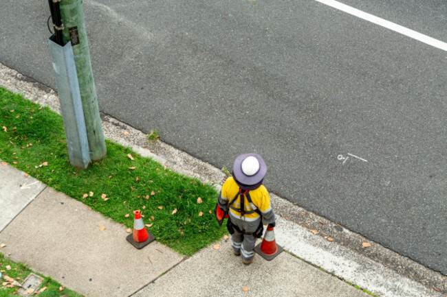 electricity-worker-standing-near-wooden-power-pole-on-street-edge