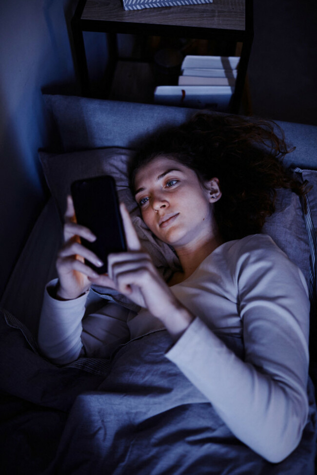 high-angle-view-of-young-woman-communicating-online-on-mobile-phone-before-sleep-lying-on-her-bed