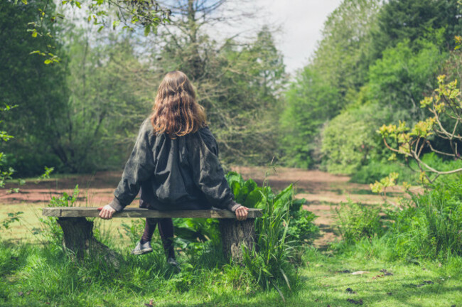 a-young-woman-is-sitting-on-a-bench-by-a-pond