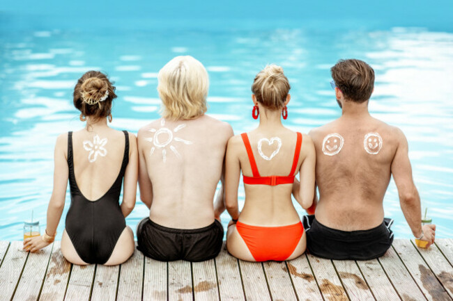 friends-with-sun-cream-painted-shapes-on-the-shoulders-sitting-together-on-the-poolside-concept-of-a-skin-protection-from-a-sun-rear-view