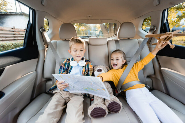 cheerful-kids-with-toys-and-map-sitting-on-back-seat-of-car