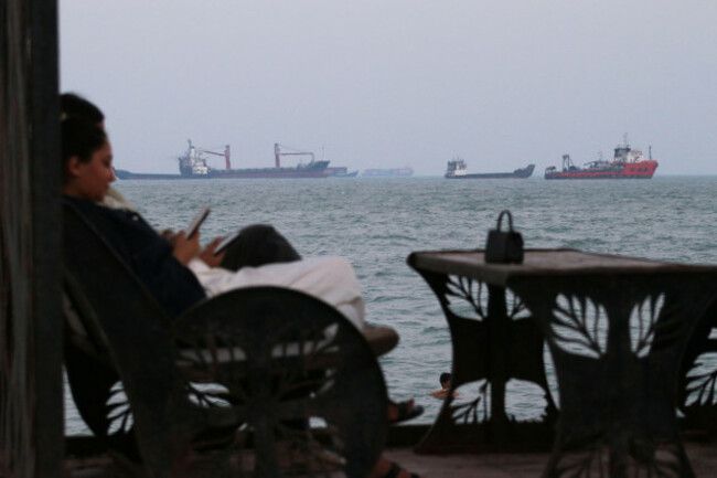 residents-check-their-cellphones-as-they-sit-at-a-cafe-overlooking-commercial-vessels-anchored-in-the-strait-of-hormuz-off-bandar-abbas-iran-sunday-july-12-2026-razieh-poudatisna-via-ap