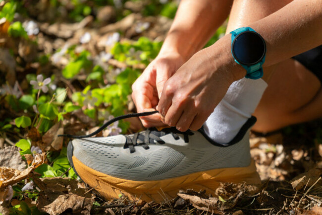 close-up-of-a-trail-runner-tying-shoelace-in-a-sunny-spring-forest-wearing-a-sport-watch-among-green-leaves-and-wildflowers