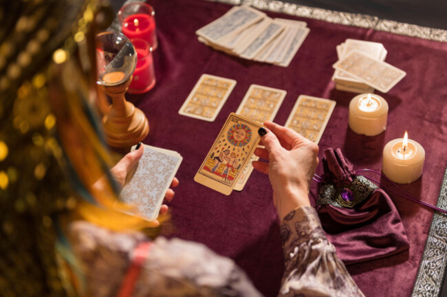 high-angle-of-crop-anonymous-female-fortune-teller-picking-sun-tarot-card-while-sitting-at-table-with-burning-candles-and-crystal